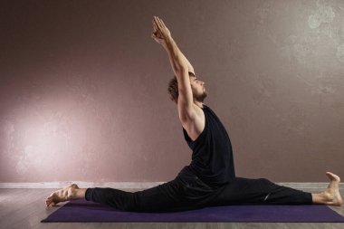 Genç sporcu yoga yapıyor, yoga pozisyonunda meditasyon yapıyor spor kıyafetleri giyiyor, kapalı alanda yoga yapıyor, kahverengi yoga stüdyosu.