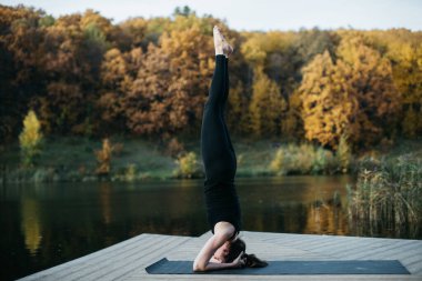 Göl manzaralı doğada yoga yapan genç bir kadın. Akşam sporu, spor ve sağlıklı yaşam tarzı.