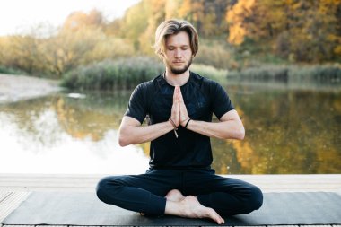 Genç adam göl manzaralı doğada yoga yapıyor. Akşam sporu, spor ve sağlıklı yaşam tarzı.