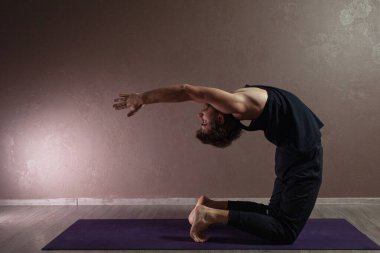 Genç sporcu yoga yapıyor, yoga pozisyonunda meditasyon yapıyor spor kıyafetleri giyiyor, kapalı alanda yoga yapıyor, kahverengi yoga stüdyosu.