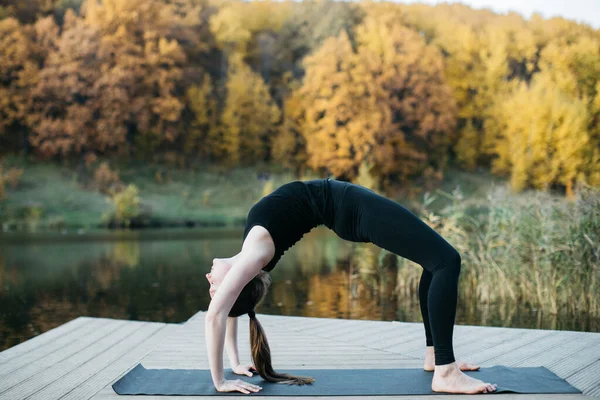 Egy fiatal nő jógázik a természetben a tóra néző kilátással. Esti edzés a szabadban, sport és egészséges életmód — Stock Fotó