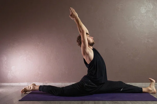 stock image Young sporty man practicing yoga, meditating in yoga pose, working out, wearing sportswear, indoor full length, brown yoga studio