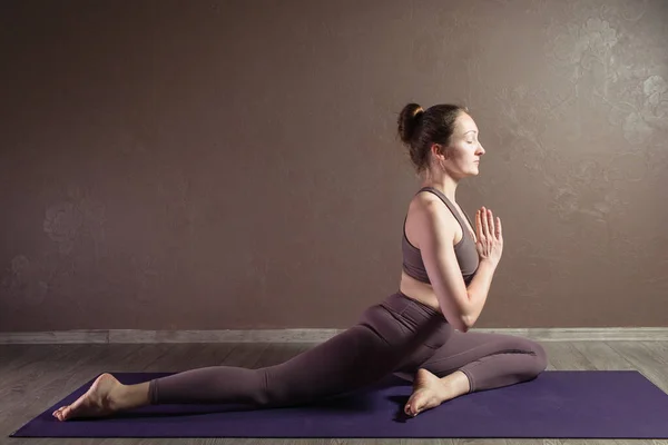 Joven mujer atractiva deportista practicando yoga, meditando en pose de yoga, haciendo ejercicio, usando ropa deportiva, estudio de yoga marrón — Foto de Stock