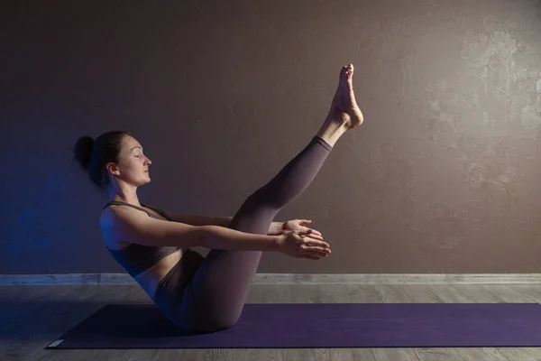 Joven mujer atractiva deportista practicando yoga, meditando en pose de yoga, haciendo ejercicio, usando ropa deportiva, estudio de yoga marrón — Foto de Stock