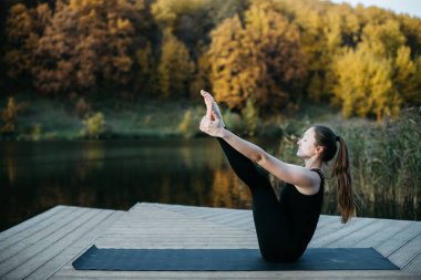 Göl manzaralı doğada yoga yapan genç bir kadın. Akşam sporu, spor ve sağlıklı yaşam tarzı.