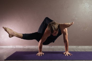 Genç sporcu yoga yapıyor, yarım Lotus pozisyonunda meditasyon yapıyor spor kıyafetleri giyiyor, kapalı alanda yoga yapıyor, kahverengi yoga stüdyosu.