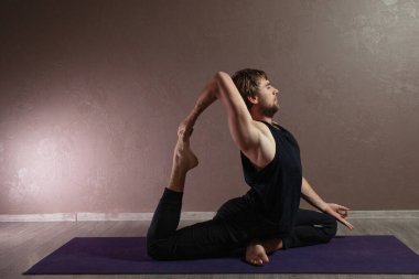 Genç sporcu yoga yapıyor, yoga pozisyonunda meditasyon yapıyor spor kıyafetleri giyiyor, kapalı alanda yoga yapıyor, kahverengi yoga stüdyosu.