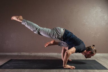 Genç sporcu yoga yapıyor, yarım Lotus pozisyonunda meditasyon yapıyor spor kıyafetleri giyiyor, kapalı alanda yoga yapıyor, kahverengi yoga stüdyosu.
