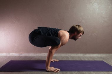 Genç sporcu yoga yapıyor, yarım Lotus pozisyonunda meditasyon yapıyor spor kıyafetleri giyiyor, kapalı alanda yoga yapıyor, kahverengi yoga stüdyosu.