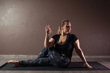 Genç sportif çekici kadın yoga yapıyor, yoga pozisyonunda meditasyon yapıyor spor kıyafetleri giyiyor, kapalı alanda yoga yapıyor, kahverengi yoga stüdyosu.