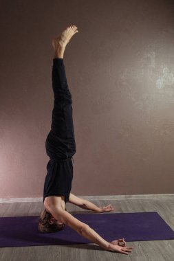 Genç sporcu yoga yapıyor, yoga pozisyonunda meditasyon yapıyor spor kıyafetleri giyiyor, kapalı alanda yoga yapıyor, kahverengi yoga stüdyosu.