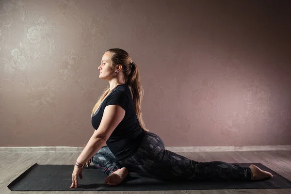 Wanita muda yang atraktif berlatih yoga, bermeditasi dalam pose yoga, bekerja keluar, mengenakan pakaian olahraga, indoor full length, studio yoga coklat — Stok Foto