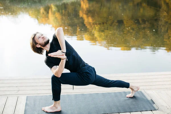Joven haciendo yoga asana en la naturaleza con vista al lago. Entrenamiento nocturno al aire libre, deportes y estilo de vida saludable — Foto de Stock