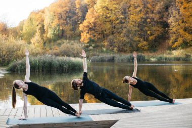 Genç kadınlar ve erkek göl manzaralı doğada yoga yapıyorlar. Akşam sporu, spor ve sağlıklı yaşam tarzı.