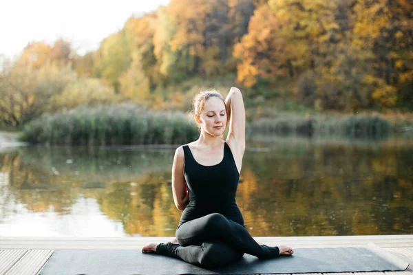 Mujer joven haciendo yoga asana en la naturaleza con vista al lago. Entrenamiento nocturno al aire libre, deportes y estilo de vida saludable — Foto de Stock