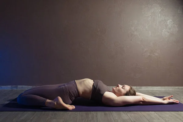 Joven mujer atractiva deportista practicando yoga, meditando en pose de yoga, haciendo ejercicio, usando ropa deportiva, estudio de yoga marrón — Foto de Stock