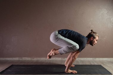 Genç sporcu yoga yapıyor, yarım Lotus pozisyonunda meditasyon yapıyor spor kıyafetleri giyiyor, kapalı alanda yoga yapıyor, kahverengi yoga stüdyosu.