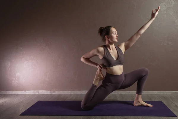 Joven mujer atractiva deportista practicando yoga, meditando en pose de yoga, haciendo ejercicio, usando ropa deportiva, estudio de yoga marrón — Foto de Stock