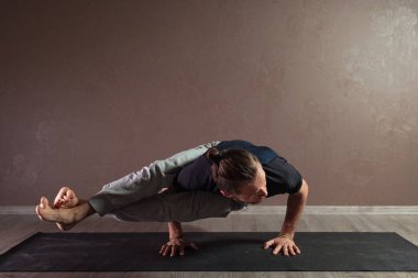 Genç sporcu yoga yapıyor, yarım Lotus pozisyonunda meditasyon yapıyor spor kıyafetleri giyiyor, kapalı alanda yoga yapıyor, kahverengi yoga stüdyosu.