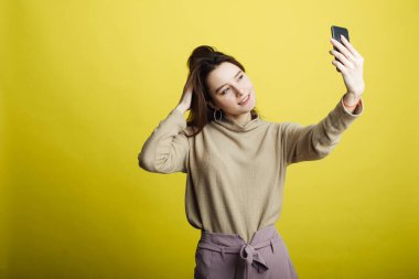 Sarı arka planda izole edilmiş, selfie çeken mutlu genç kız görüntüsü.