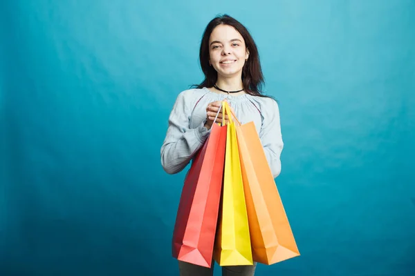 Image of happy young girl standing on blue background with shopping bags — Stock Photo, Image