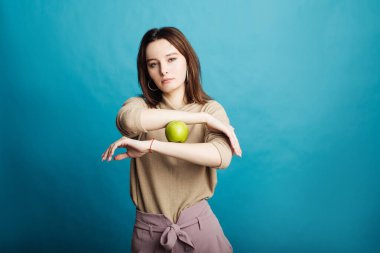 Mavi bir arka planda elinde yeşil bir elma tutan mutlu bir genç kız resmi.