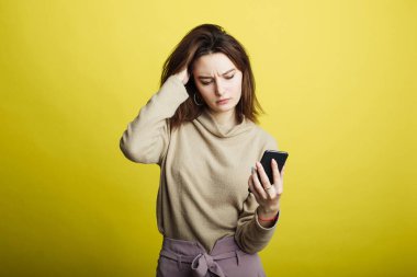 Sarı arka planda izole edilmiş, telefondan mesajlar okuyan mutlu genç kız görüntüsü