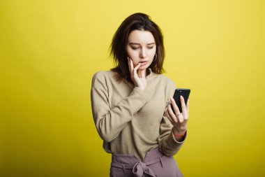 Sarı arka planda izole edilmiş, telefondan mesajlar okuyan mutlu genç kız görüntüsü