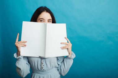 Mavi bir arka planda elinde bir dergiyle duran mutlu genç bir kızın görüntüsü.