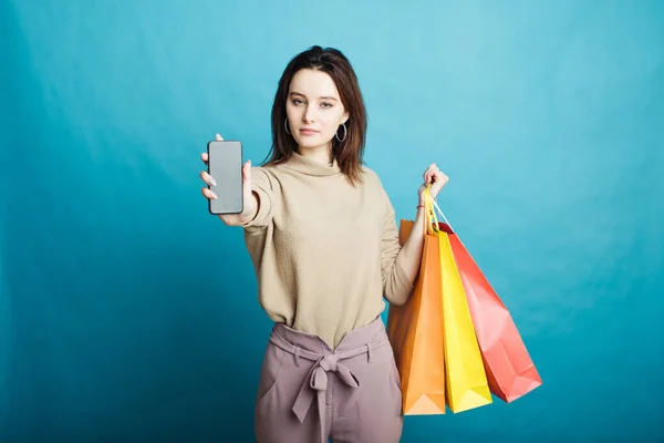 Image of happy young girl standing on blue background with shopping bags and phone — Stock Photo, Image