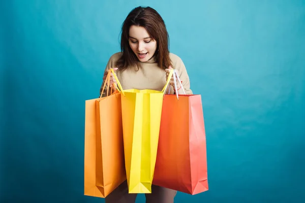 Image of happy young girl standing on blue background with shopping bags — Stock Photo, Image