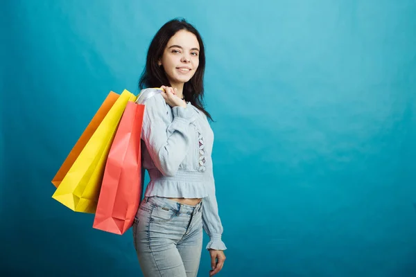 Image of happy young girl standing on blue background with shopping bags — Stock Photo, Image