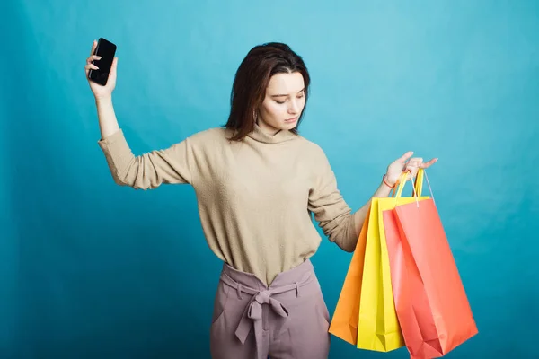 Immagine di felice ragazza in piedi su sfondo blu con borse della spesa e telefono — Foto Stock