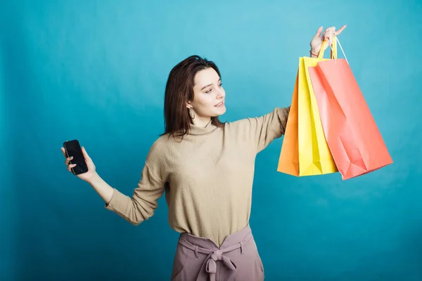 Image of happy young girl standing on blue background with shopping bags and phone — Stock Photo, Image