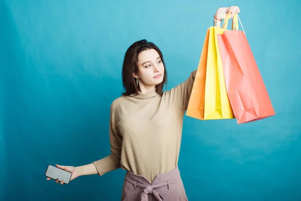 Image of happy young girl standing on blue background with shopping bags and phone — Stock Photo, Image