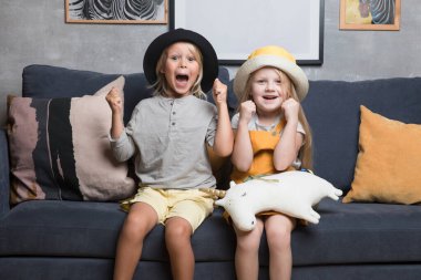 Bir erkek ve bir kız mavi bir kanepeye oturur ve farklı duygular gösterirler. Çocuklar