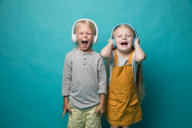 Very emotional children listen to music with headphones on a blue background. Boy and girl are dancing and showing different emotions and he is happy