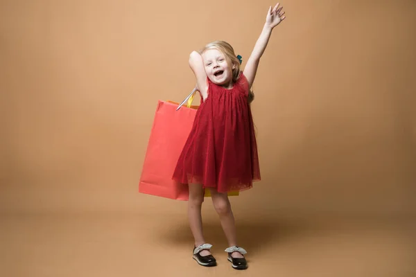 A young girl in a red dress and with shopping bags, very happy shopping. A young girl stands on an orange background — Stock Photo, Image