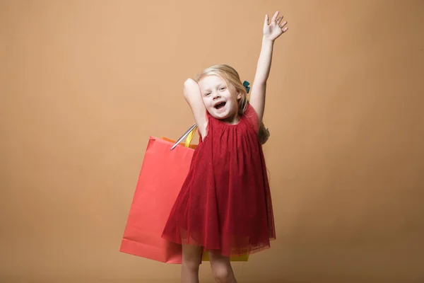 Une jeune fille en robe rouge et avec des sacs à provisions, très joyeux shopping. Une jeune fille se tient sur un fond orange — Photo