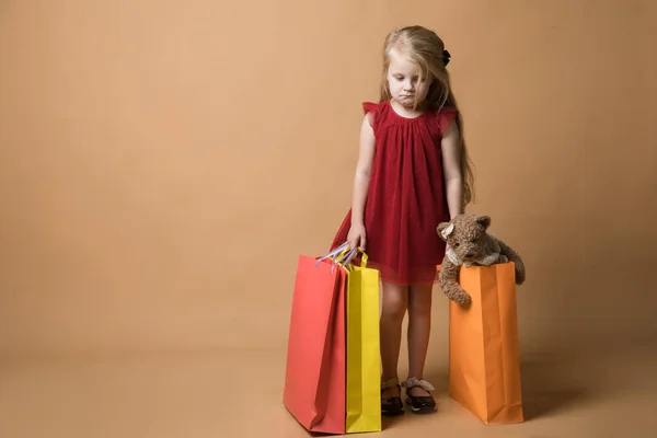 一个穿着红衣服，提着购物袋的小女孩，很开心地购物。 一个年轻姑娘站在橙色的背景上 — 图库照片