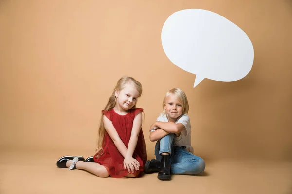 Un garçon et une fille s'assoient par terre sur un fond orange. Les enfants sont très heureux. Des enfants suspendus blanc blanc discours — Photo