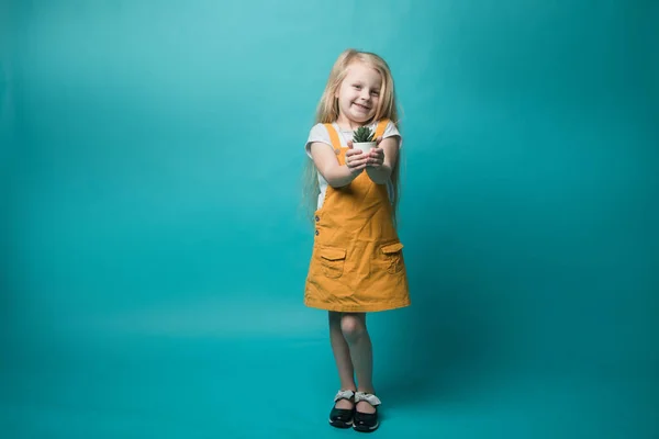 Une petite fille tenant des pots avec une plante verte sur un fond bleu. Enfants et nature. Préserver la nature — Photo