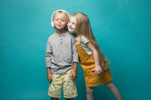 Very emotional children listen to music with headphones on a blue background. Boy and girl are dancing and showing different emotions and he is happy — 图库照片