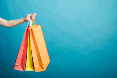 An image of a girls hand holding shopping bags standing isolated on a blue background
