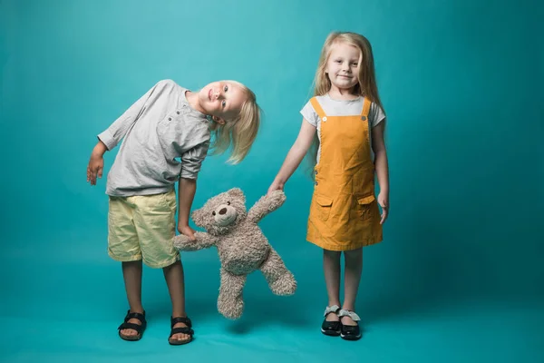 Garçon et fille sur fond bleu, tenant dans leurs mains un ours gris. Les enfants sont très joyeux. Jouets — Photo