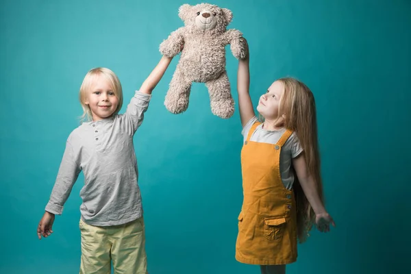 Garçon et fille sur fond bleu, tenant dans leurs mains un ours gris. Les enfants sont très joyeux. Jouets — Photo