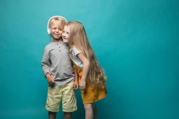 Very emotional children listen to music with headphones on a blue background. Boy and girl are dancing and showing different emotions and he is happy — 图库照片