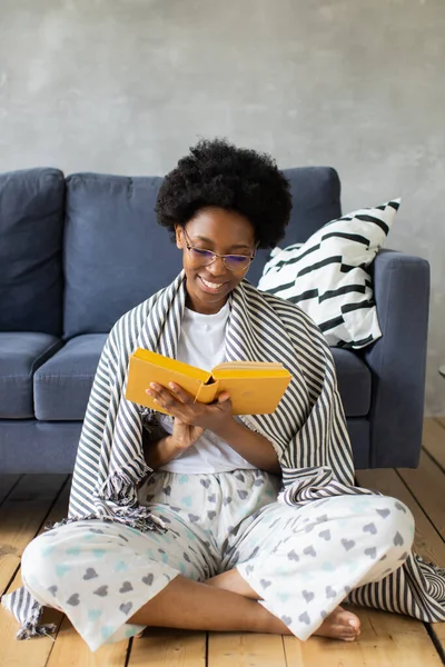 Happy African American young woman sit relax on cozy couch and reads a book. Happy to move to new apartment.