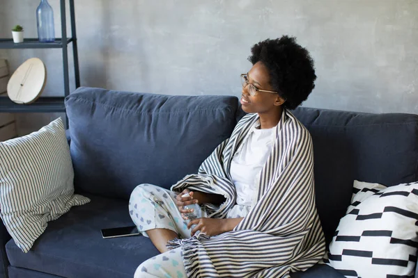Happy african American young woman sit relax on cozy couch happy to move to new apartment. Smiling black girl rest on comfortable sofa in living room dreaming