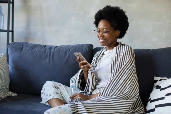 Happy african American young woman sit relax on cozy couch happy to move to new apartment. Smiling black girl rest on comfortable sofa in living room dreaming